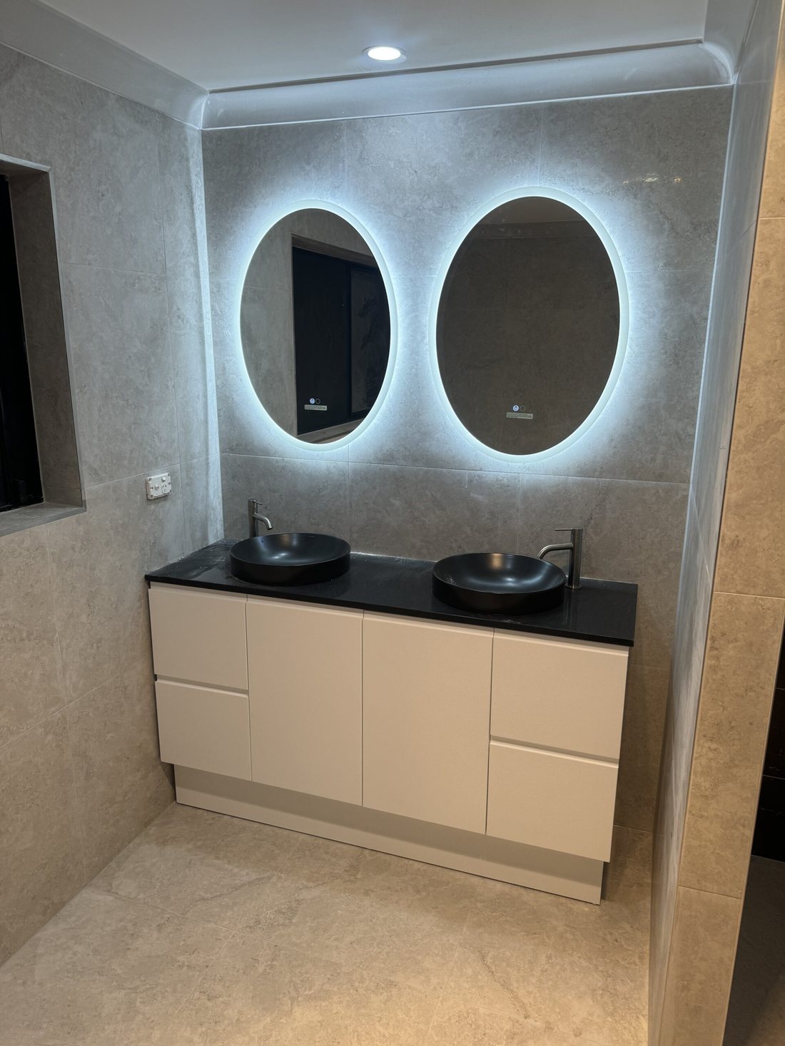 A2Z bathroom with twin backlit oval mirrors, black vessel basins and a white double vanity